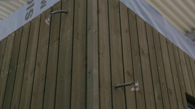 Close-up of vertical wooden exterior cladding on a prefab house wall with exposed electrical conduits and connectors
