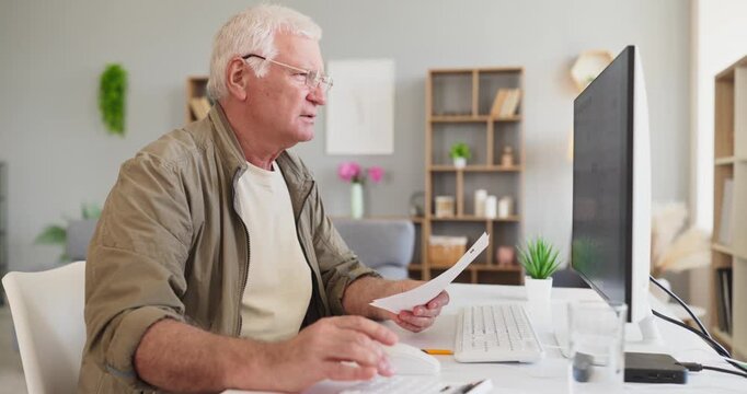 Senior elderly man reviewing electricity bill on computer. At a home office he checks utilities invoice and plans payment, tracking costs and monthly usage. Clear budgeting and savings concept.