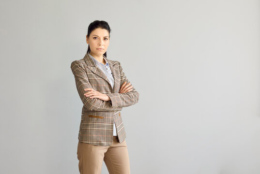 Businesswoman portrait of a confident corporate leader. Serious female manager and executive with arms crossed against gray background with copy space. Concept of authority, focus and success.