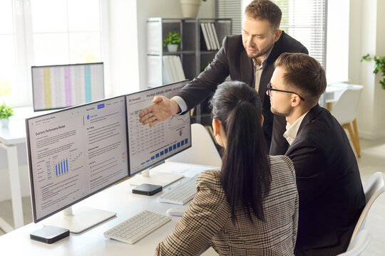 Business coworkers in office meeting analyzing data. Manager guides team at screens to review analytics and plan strategy during discussion. Clear concept of collaborative data teamwork.
