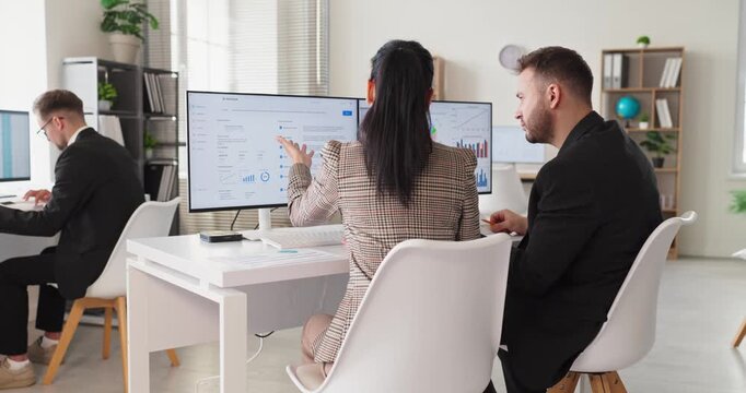 Business colleagues analysts in office discuss data. They analyze charts on dual computer monitors and work with a manager to align strategy and boost growth. Teamwork and data analysis concept.