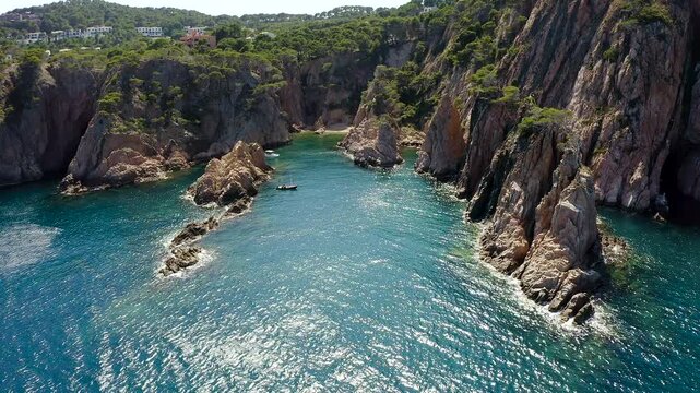 Aerial view of Cala Marquesa with boats, featuring spectacular rocky cliffs, narrow sea fissures, rugged islets and the crystal-clear Mediterranean waters of the Costa Brava. 