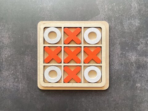 Wooden tic tac toe board game with X and O pieces representing strategy, planning, competition and decision making.