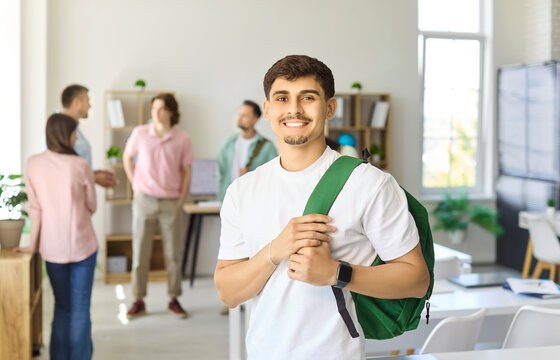 Student male in classroom group discussion. Smiling learner with backpack in study room as peers talk, useful for college and university learning use. Strong concept of student teamwork.