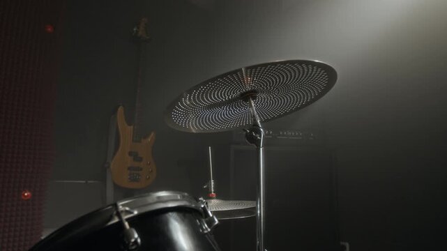 Drum kit with perforated cymbal standing in dark music rehearsal studio as camera pans slowly. Video for music school promotions or band advertisements