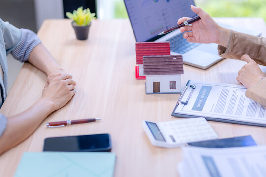 Real estate agent pointing at a laptop dashboard to explain housing loan trends and contract agreement details to a client.