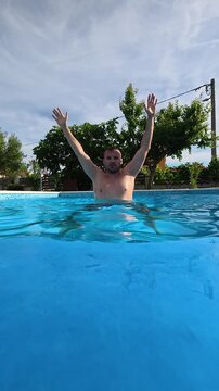 Man performing jumping jack exercises in a swimming pool. Fitness concept of water aerobics, aquatic training, healthy lifestyle, and outdoor exercise.