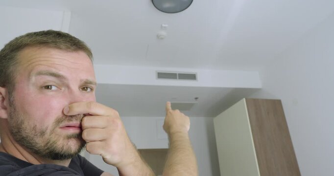 Man holding his nose because of a bad smell coming from the hotel room air conditioning. Travel concept of poor room hygiene, unpleasant odors, ventilation problems, and accommodation complaints.