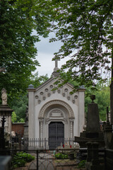 Fototapeta premium An ancient stone crypt stands among green trees in an old cemetery. This historic burial vault building represents religious architecture, family heritage, memorial services, and gothic sorrow.