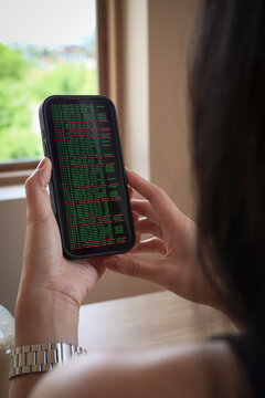 A vertical of a person holding a smartphone showing green and red programming code text. Concept of mobile hacking, cyber security breach, data analysis, and coding log.