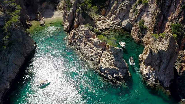 Aerial view of Cala Marquesa with boats, featuring spectacular rocky cliffs, narrow sea fissures, rugged islets and the crystal-clear Mediterranean waters of the Costa Brava. 