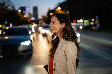 Fototapeta premium Smiling woman standing on city street at night