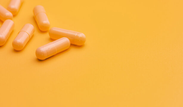 Yellow capsule pills on yellow background with space. Pharmacy and health insurance concept. Prescription drug. Pharmaceutical industry. Vitamins and supplements. Online pharmacy. Health promotion.