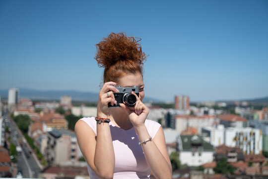 Young redhead woman photographer phototographing city from a building rooftop on a sunny summer day