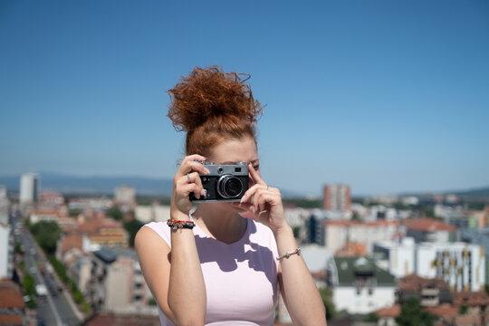 Young redhead woman photographer phototographing city from a building rooftop on a sunny summer day
