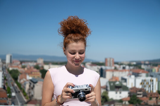 Young redhead woman photographer phototographing city from a building rooftop on a sunny summer day