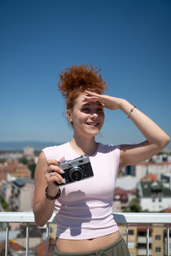 Young redhead woman photographer phototographing city from a building rooftop on a sunny summer day