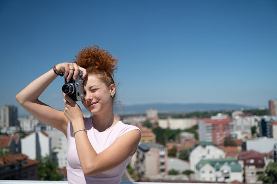 Young redhead woman photographer phototographing city from a building rooftop on a sunny summer day