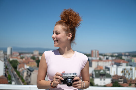 Young redhead woman photographer phototographing city from a building rooftop on a sunny summer day