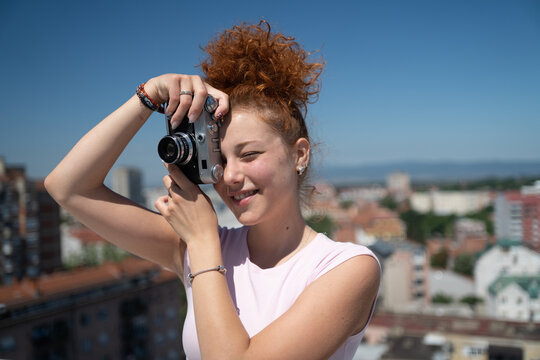 Young redhead woman photographer phototographing city from a building rooftop on a sunny summer day