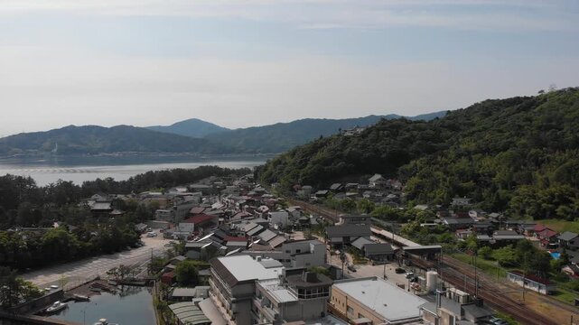 Aerial drone view descending over the coastal town and overlooking Amanohashidate Station in Kyoto, Japan