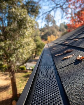 Gutter guard installation on asphalt shingle roof in autumn landscape view from above angled close up maintenance