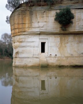 Riverfront Cliff Dwelling with Doorway and Reflection in Water in Italy Landscape View