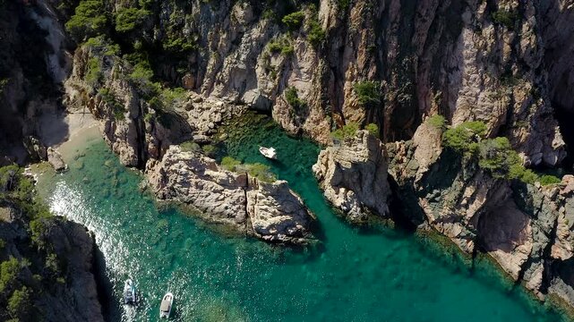 Aerial view of Cala Marquesa with boats, featuring spectacular rocky cliffs, narrow sea fissures, rugged islets and the crystal-clear Mediterranean waters of the Costa Brava. 