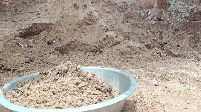 Worker digging sand and soil with a hoe tool at a construction site