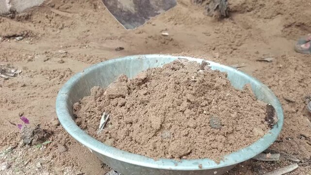 Worker digging sand and soil with a hoe tool at a construction site