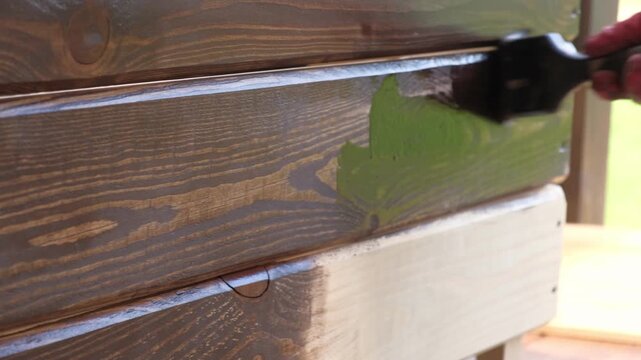 Brown oil for protection of wood by staining. Painting fence for protecting and pests. Woodworker applying finish to pine board box. Repairman varnishing with brush wooden fencing wall plank surface.
