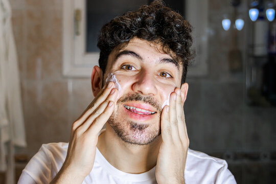 Young man smiling while applying facial cleanser foam for healthy skin and morning hygiene