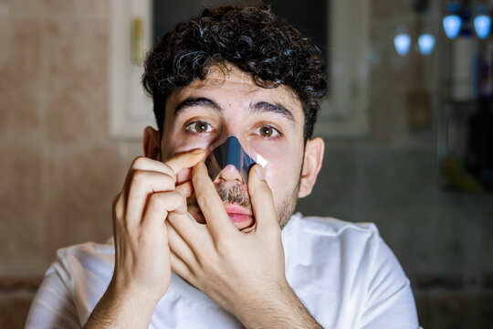 Young man taking care of his skin, applying a pore cleansing nose strip