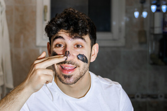 Young man applying charcoal face mask for male grooming and self-care routine