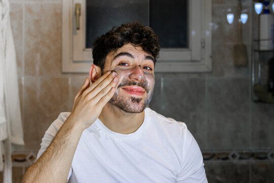 Young man applying a purifying face mask for self-care and male grooming routine