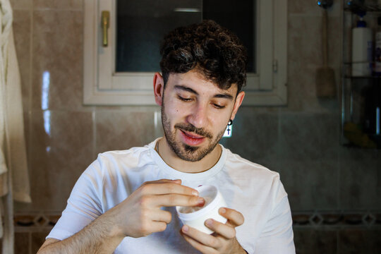 Young man applying facial cream in bathroom for daily skincare and grooming routine