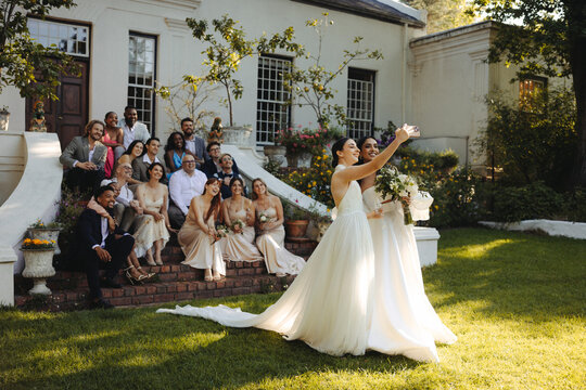 Two joyful brides taking a selfie with their wedding party outdoors