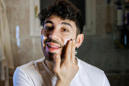 Young man applying facial cream in bathroom for self-care and grooming routine