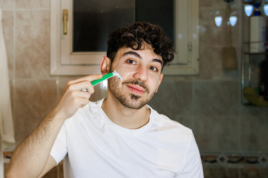 Young man shaving his face in bathroom, practicing daily self-care routine