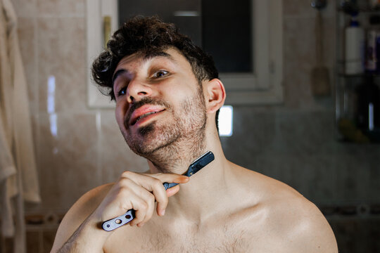 Man shaving beard with a strait razor in the bathroom, practicing self-care and grooming