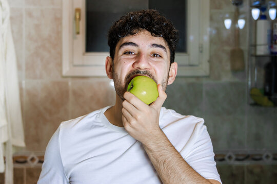 Young man biting fresh green apple, practicing healthy eating and wellness concept