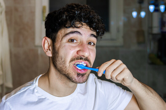 Young man caring for oral hygiene by brushing teeth in bathroom morning routine