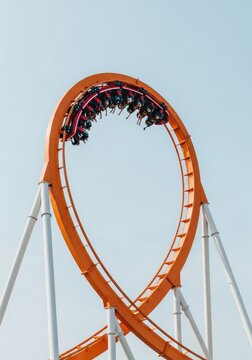 Thrilling Orange Roller Coaster Loop with People Upside Down Against a Clear Blue Sky in an Amusement Park