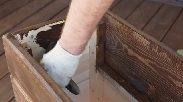 Brown oil for protection of wood by staining. Painting fence for protecting and pests. Woodworker applying finish to pine board box. Repairman varnishing with brush wooden fencing wall plank surface.