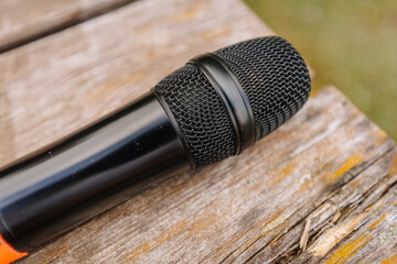 Obraz premium Close-up of a black handheld microphone resting on a weathered wooden surface with visible grain and texture, showcasing its mesh head and grip design