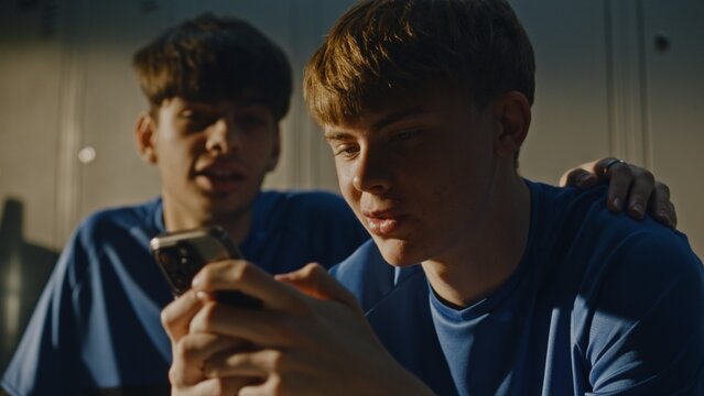 Young Soccer Players in Uniforms in Dressing Room, Sharing Content on Smartphone. One Boy Was Browsing Phone When Teammate Joined For Friendly Chat. Boys Smiling and Discussing Something on Screen.