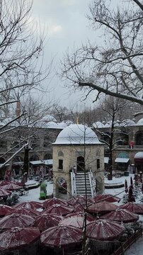 Snow-Covered Koza Han Courtyard with Red Cafe Umbrellas and Bare Winter Trees in Bursa, Turkey