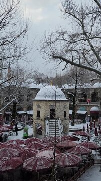Snow-Covered Koza Han Courtyard with Red Cafe Umbrellas and Bare Winter Trees in Bursa, Turkey