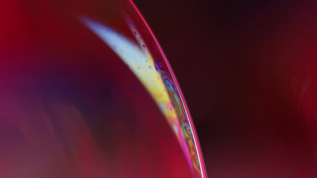 Deep crimson fluid surface macro with glowing spectral boundary arc. Abstract horizontal macro photography of a structured fluid interface.