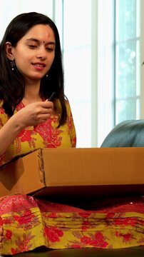 Indian Asian excited young girl in her twenties, dressed in salwar kameez, expressing surprise and happiness while unboxing a cardboard parcel with something delightful inside